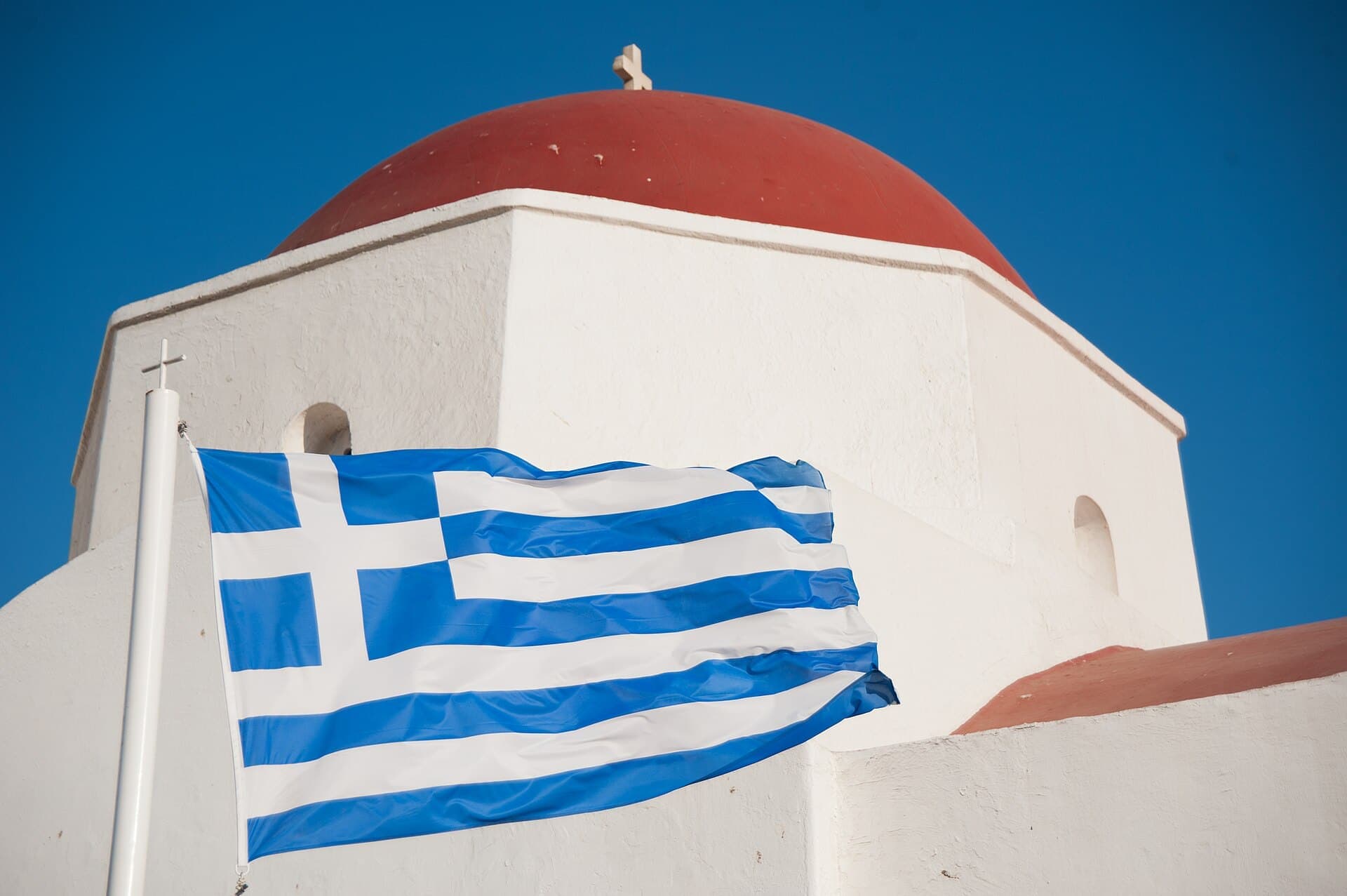 The Greek flag in front of a red-domed chapel on Mykonos